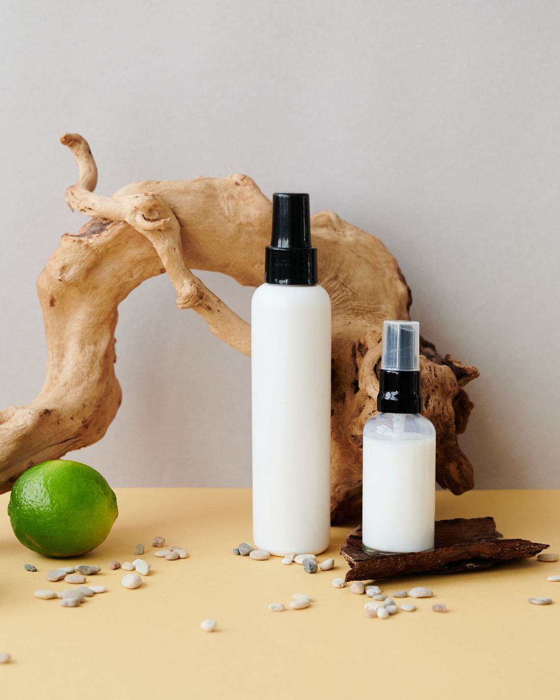 Natural cosmetic bottles beside driftwood and a lime